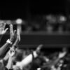 Black and white image of audience with hands raised, capturing concert energy.